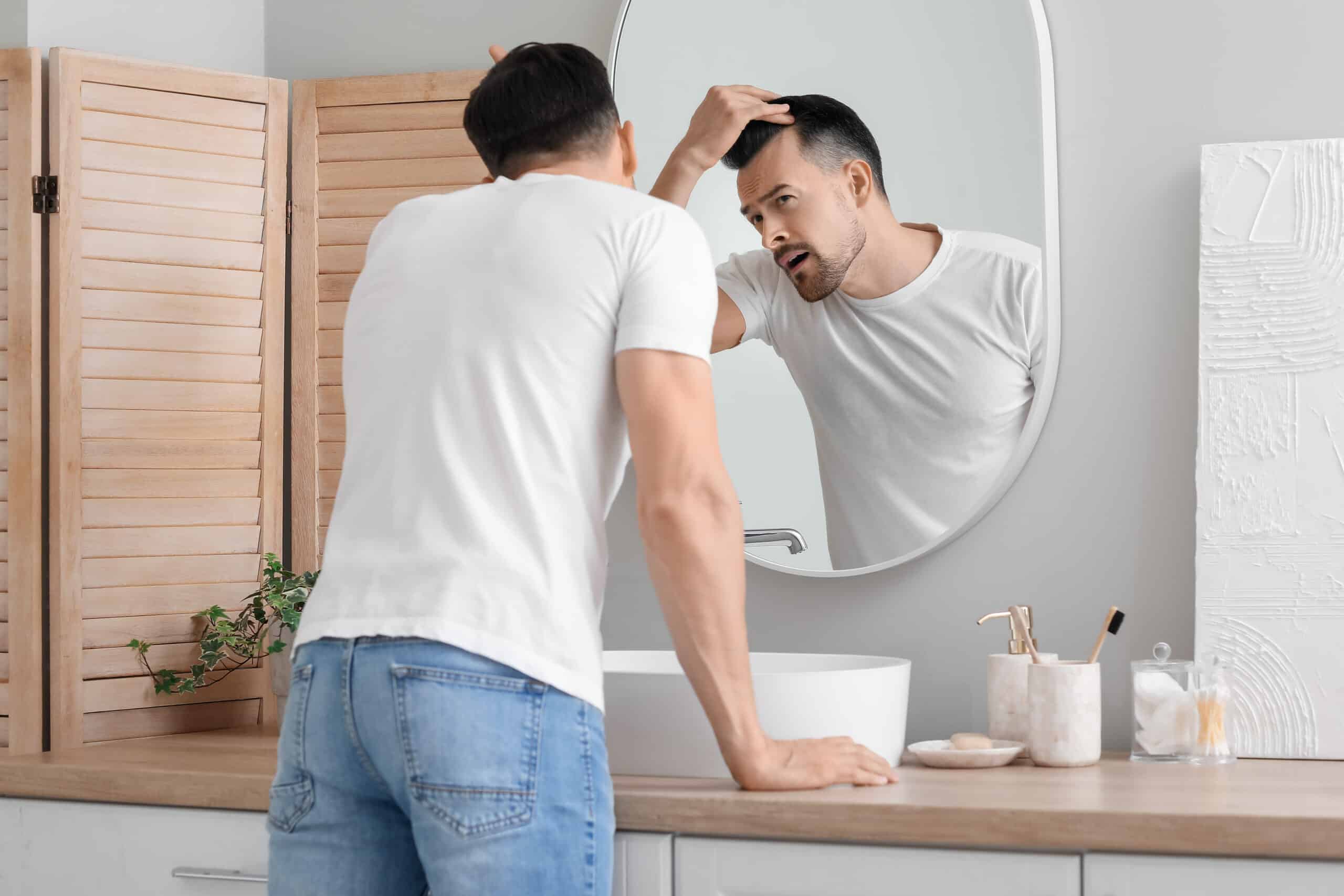 Man suffering from hair loss looking in the mirror