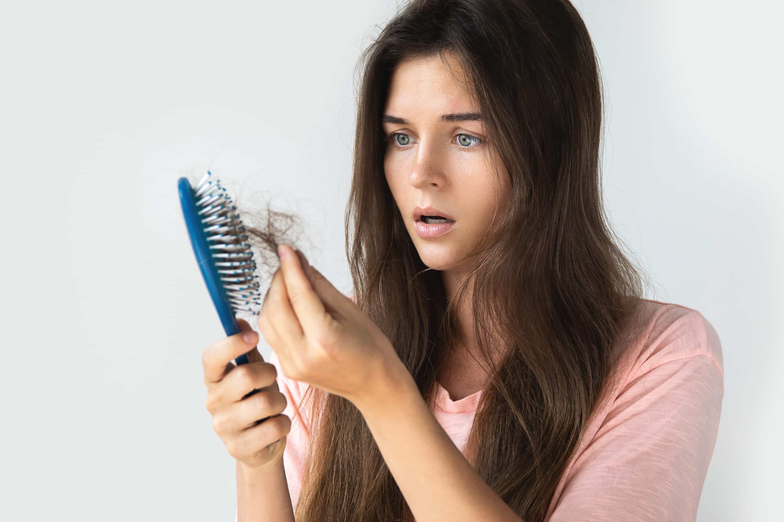 Woman in shock from hair loss, looking at strands of hair on brush.
