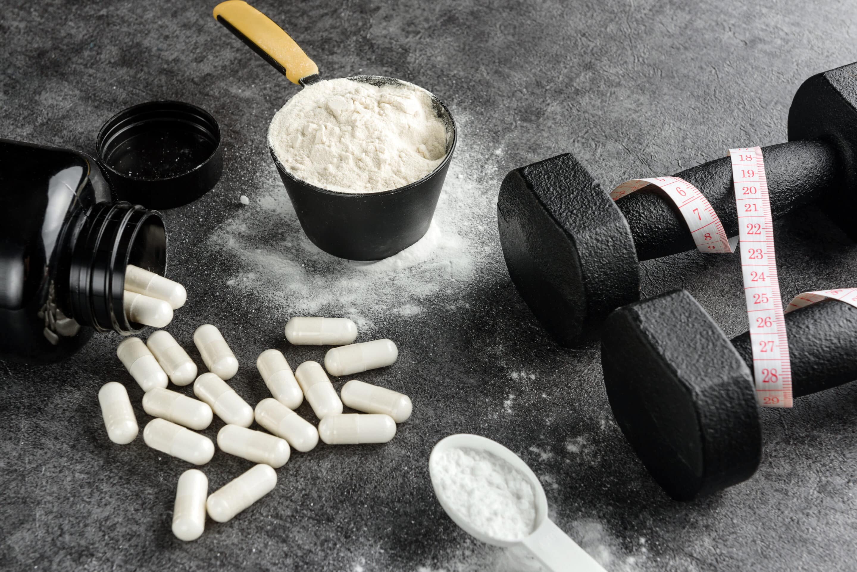 Creatine next to a set of dumb bells with a measuring tape wrapped around it.